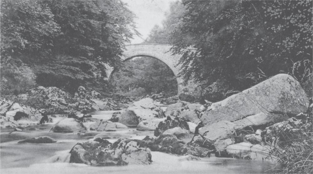 Black and white photograph of Deveron Bridge, surrounded by trees, with a rocky river flowing under it.