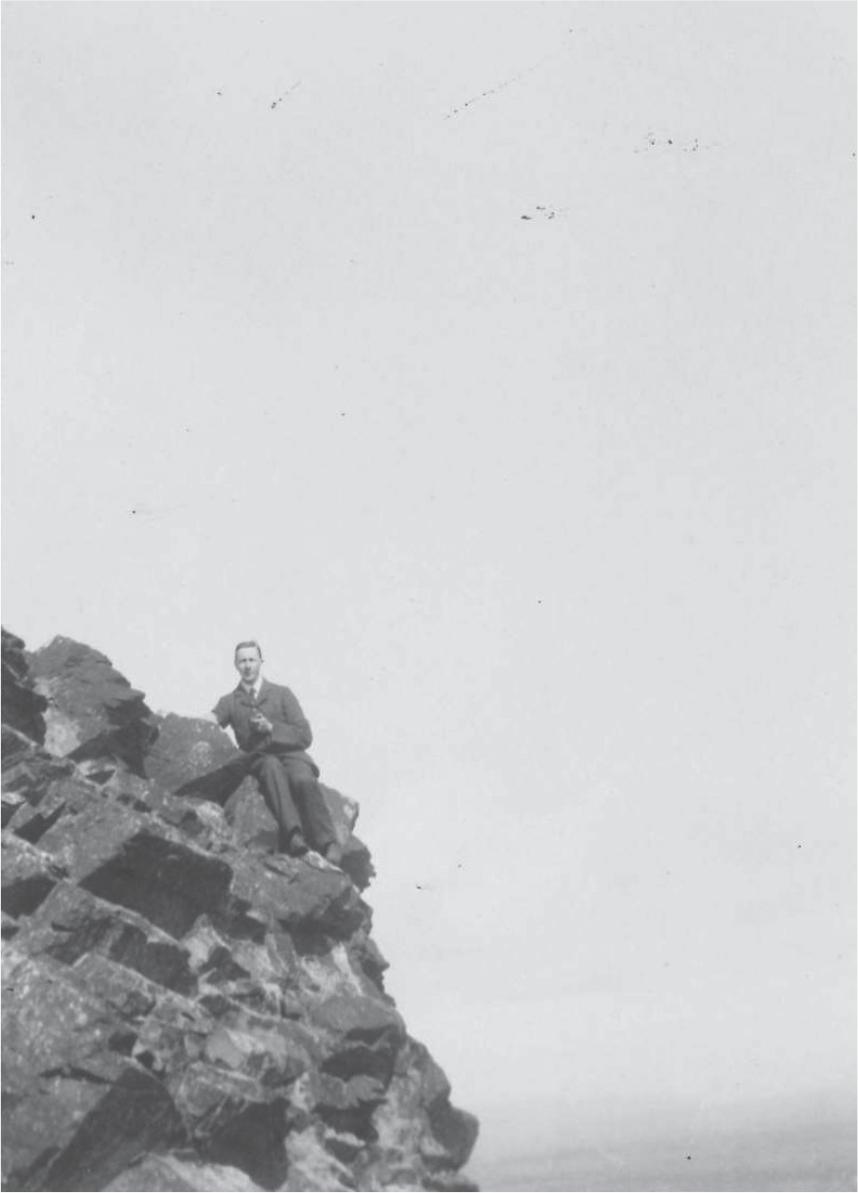 Black and white photograph of Alexander Mackie sitting on the edge of a rocky outcrop, wearing a suit and tie.