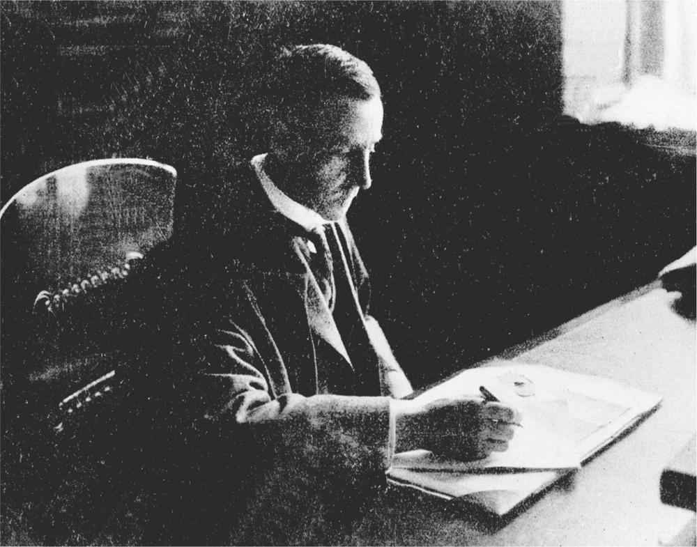 Black and white photograph of Alexander Mackie writing on a piece of paper at his desk.