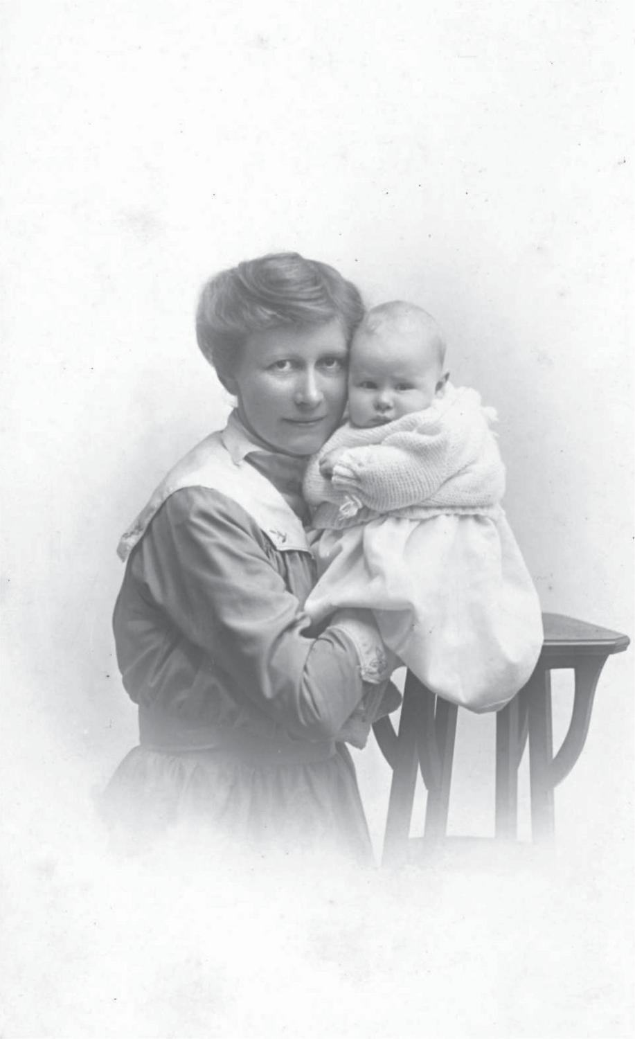 Black and white photograph of Annie holding baby John, who sits on a high wooden stool.
