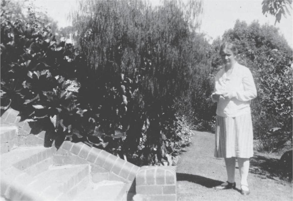 Photograph of Margaret Mackie standing beside a small tree. A set of paved steps rises in the foreground.