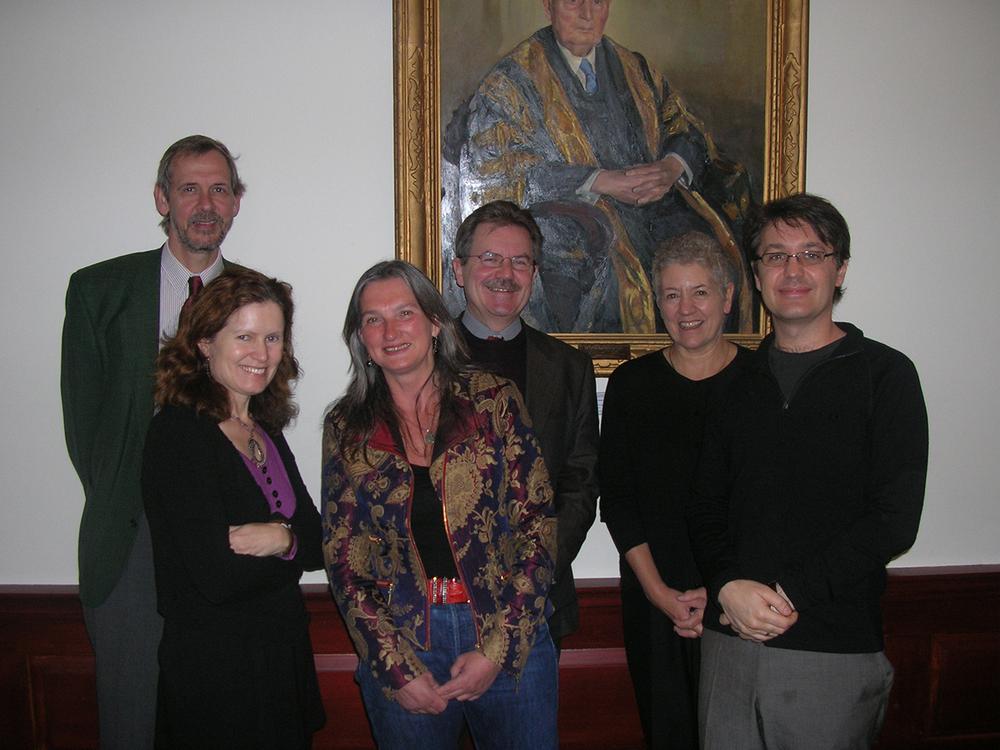 Photograph of six people standing in front of a large portrait in a gold frame.