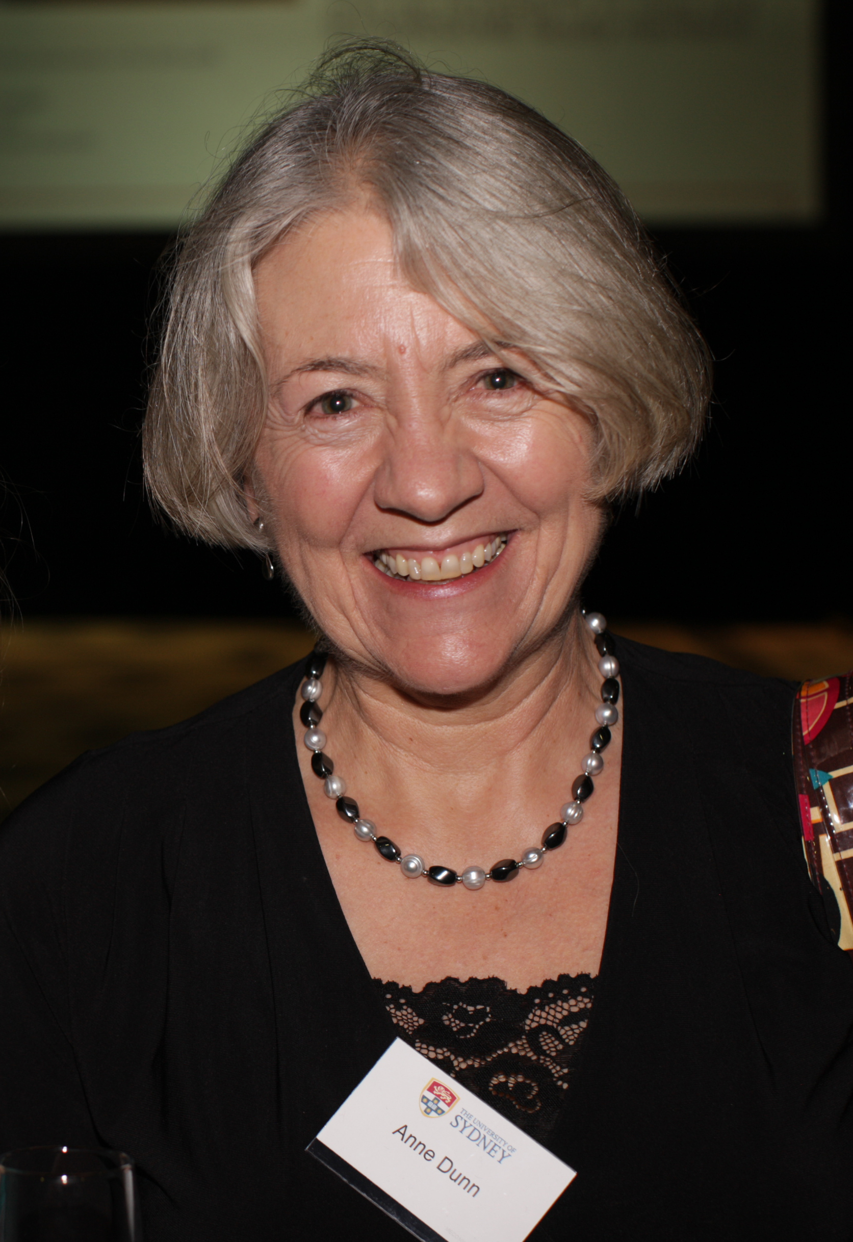 Photograph of a woman with grey hair, wearing a black top and a name tag.