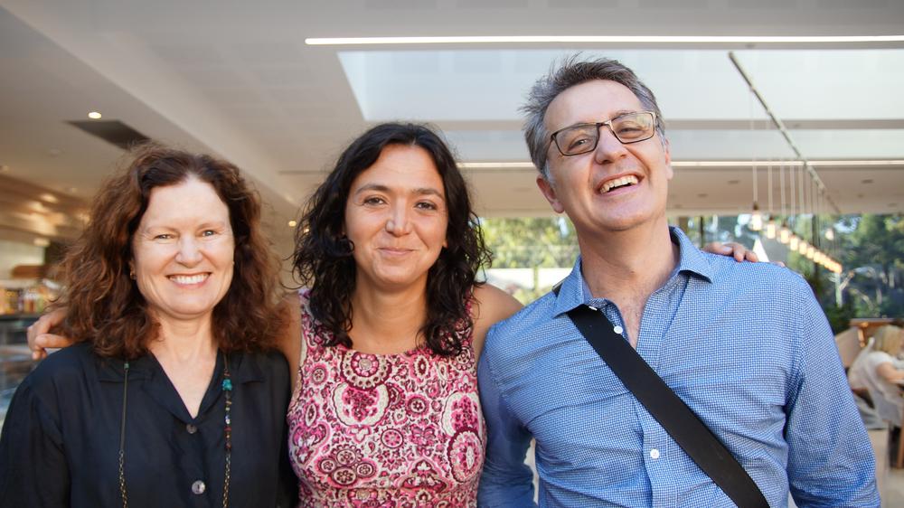 Photograph of two women and a man standing together, smiling at the camera.