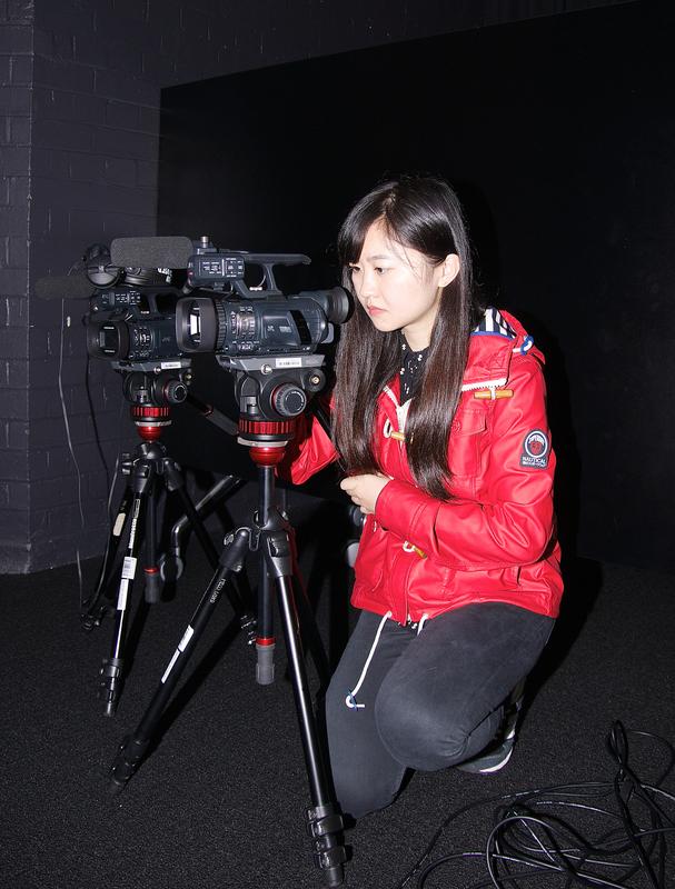 Photograph of a student kneeling behind a camera on a tripod.