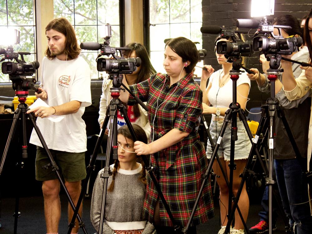 Photograph of a group of people standing behind four cameras on tripods; four people are operating the cameras, while the others watch.