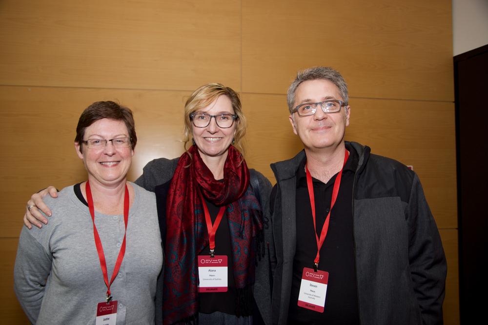 Photograph of three people standing together, wearing red lanyards and smiling at the camera.