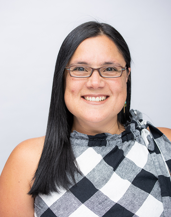 Photograph of a woman with black hair, wearing glasses and a checked top.