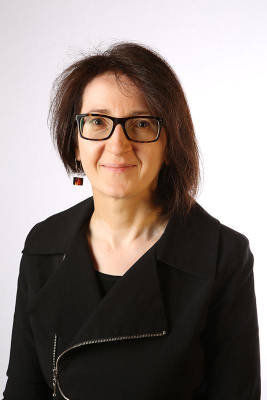 Photograph of a woman with brown hair, wearing glasses and a black jacket.
