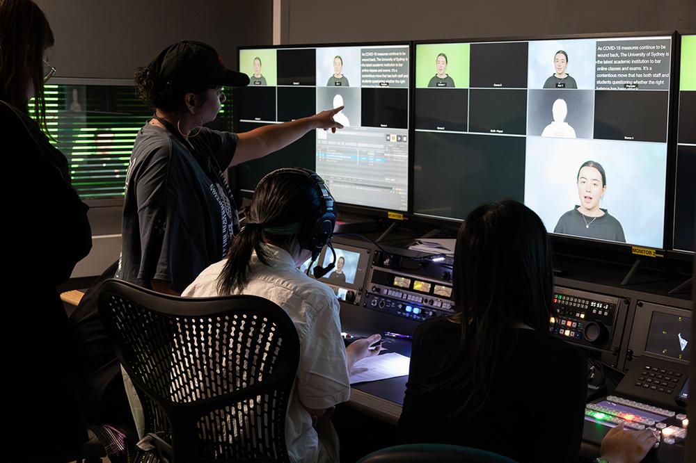 Photograph of four people, two sitting and two standing, looking at two large screens.
