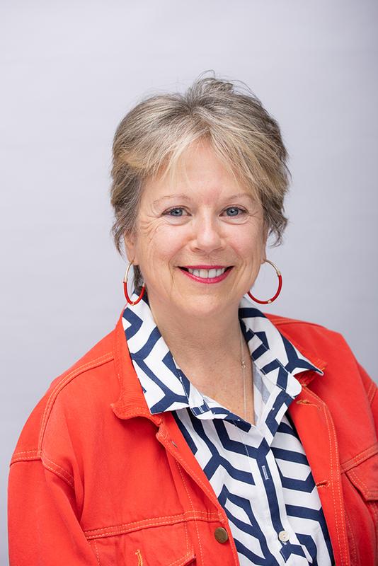 Photograph of a woman with short hair, wearing a patterned shirt and a red jacket.
