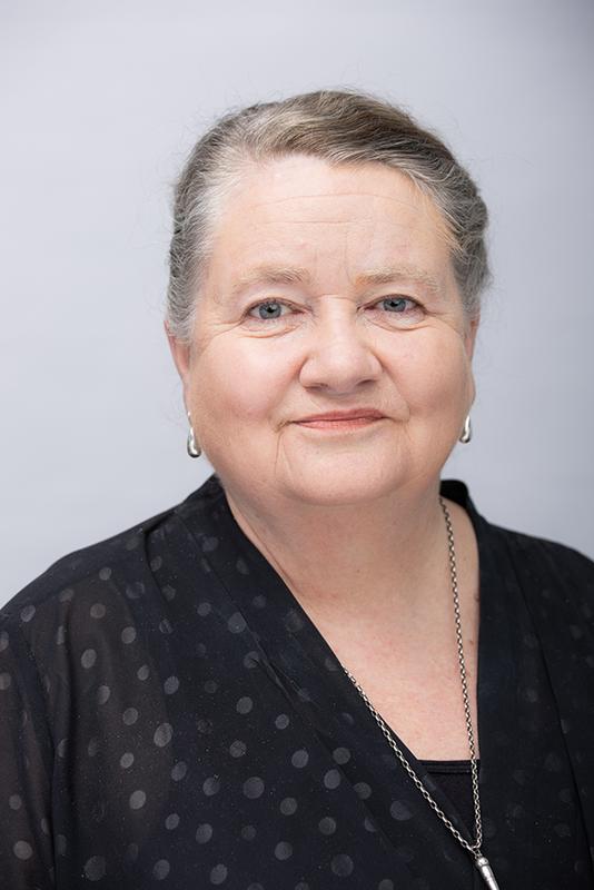 Photograph of a woman with grey hair, wearing a black top.