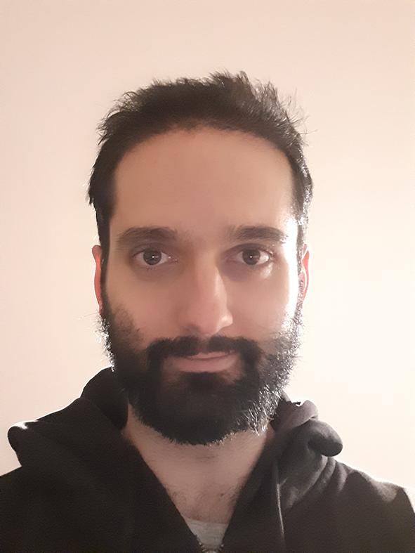 Photograph of a man with dark hair and a beard, wearing a black top.