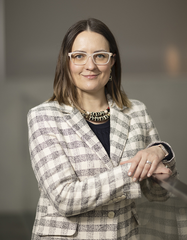 Photograph of a woman with brown hair, wearing a checked blazer and a black top.