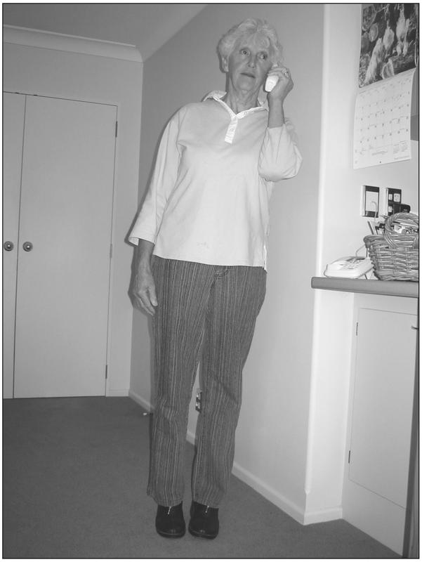 A black and white photograph of an elderly woman leaning to the side in a room with a phone raised to her ear.