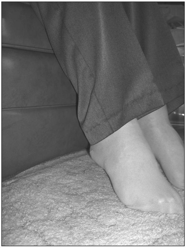 A black and white photograph of an elderly person sitting with their toes pointing to the ground.