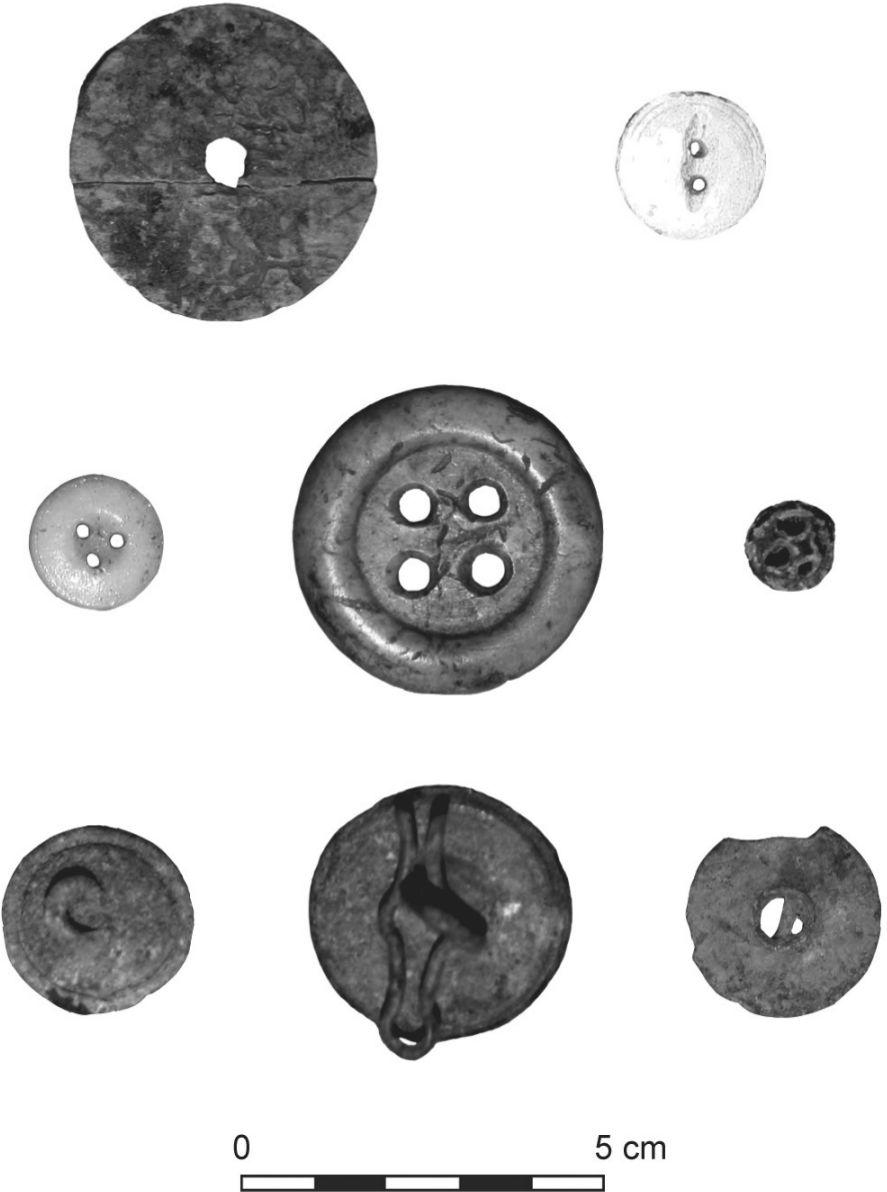A black and white photograph of eight buttons of varying sizes and designs.