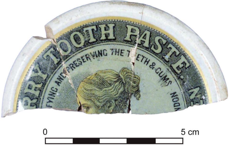 A photograph of a half broken jar. The words 'tooth paste' can be seen and the profile of a woman on a pale green background.