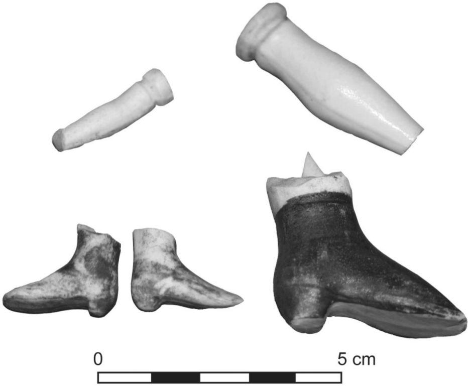A black and white photograph of doll parts. A pair of feet and a large foot wearing a dark shoe is photographed. The other two pieces appear to be a piece of an arm or leg.