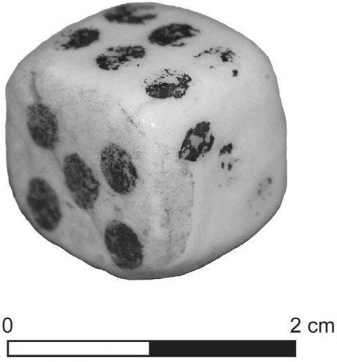 A black and white photograph of a die. Its dots are faded on some faces but the five and six sides can be seen.