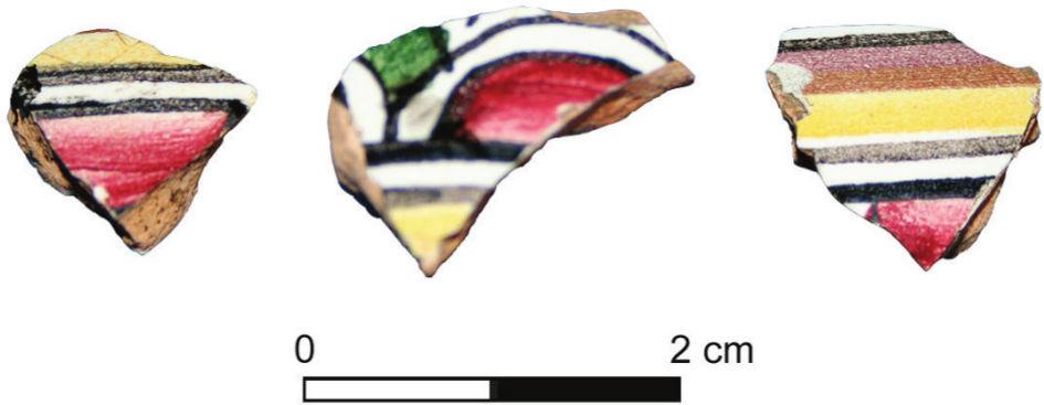A photograph of three shards from an earthenware vessel. Two pieces have a red, black and yellow striped pattern whilst the other has a scale pattern with a touch of green.