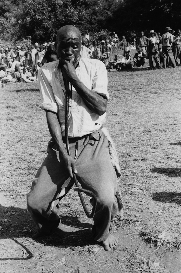 Figure 6.3. A black and white image of a middle-aged man playing a nanga flute in front of onlookers.