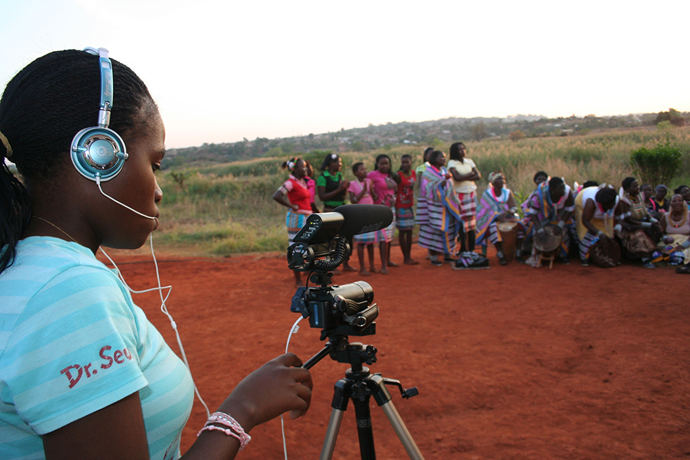 Figure 7.8. A teenaged girl wearing headphones uses a video camera to record dancers. The attention of the people in the background is focused away from her, on the unseen dancers.