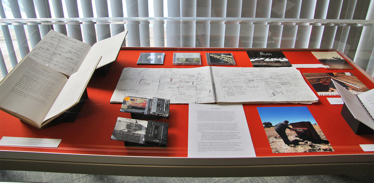 Figure 9.3. Items in a display case include handwritten notebooks, sheet music, cassette tapes, CDs, books, and a photo of a man playing a piano in the desert.