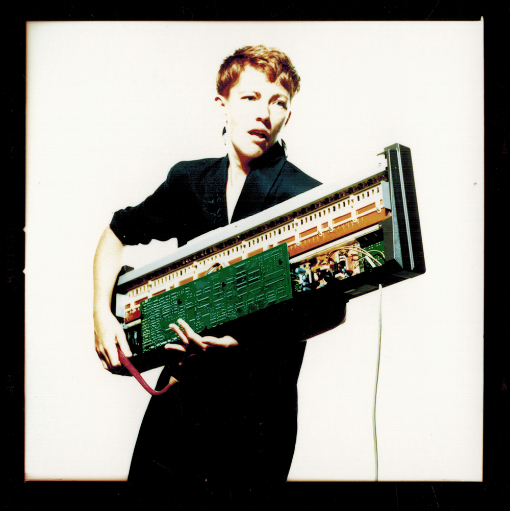 Figure 9.1. An orange-haired woman wears a black dress and holds an eighties-style keyboard with the electronics showing.