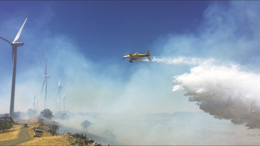 Water-bombing aircraft flying over a windfarm.