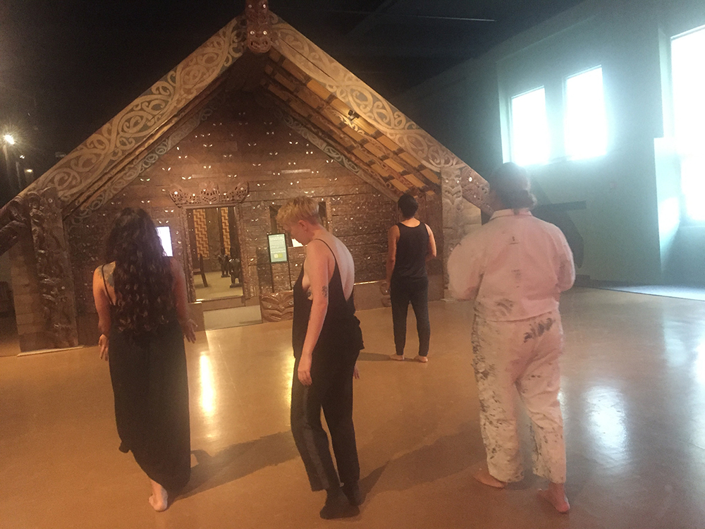 Jack Gray (in overalls) and the dancers cross an open floor section in the museum intended to represent the atea, a spatial threshold in front of a house intended to represent the atua named Tūmatauenga – the entity of warfare and human conflict.