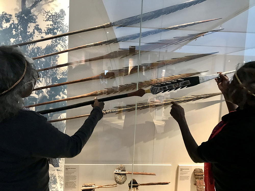 Two Tiwi women view a display of six Tiwi spears at the Chau Chak Wing Museum. The woman on the left of the image holds a seventh spear.