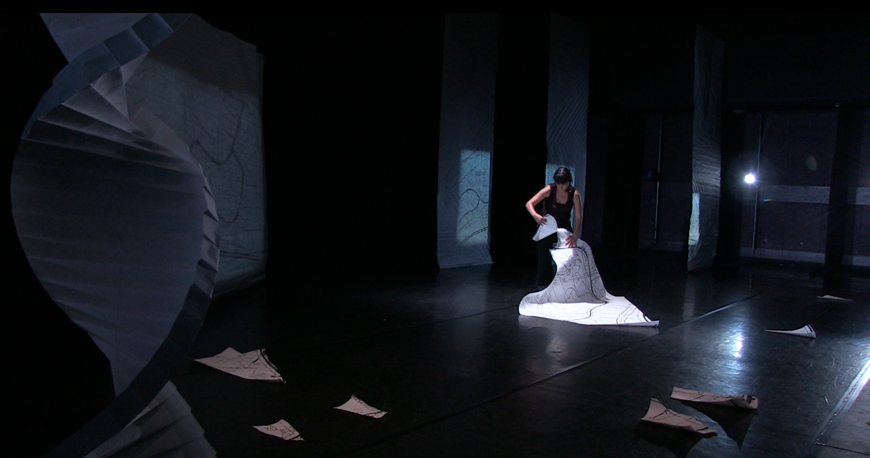 Rosy Simas tears up a large map on a stage. Pieces of torn paper litter the floor.