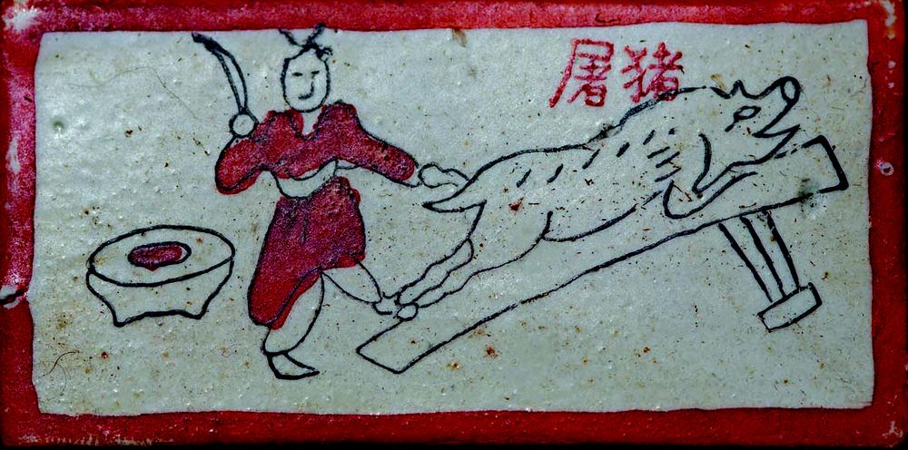 Rectangular pictograph with a red border showing a simple line drawing of a person holding a knife next to a pig lying on a slanted bench. A round table with a bowl is on the left. Chinese characters appear in the top right corner. 