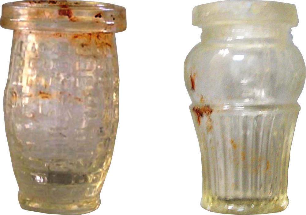 Two small jars, isolated against a white background. The first is rounded with a pronounced lip at the top. The second has a narrow, tapered base with vertical ridges, a smooth and bulbous shoulder, and wide opening with a pronounced lip.