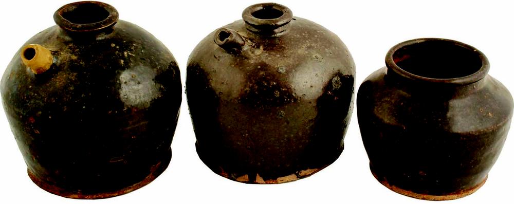 Three storage vessels in a row, isolated against a white background. The first two vessels have large shoulders, a small opening and a spout on the left side. The third vessel is smaller and has a much wider opening. 