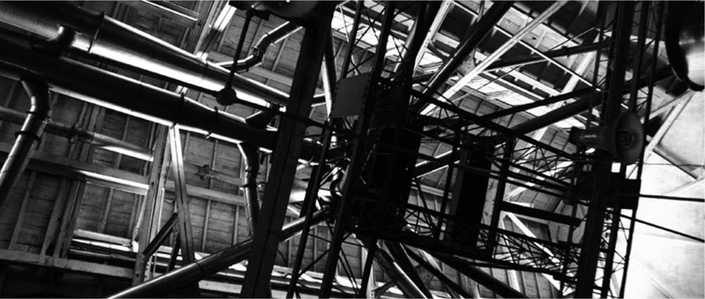 A black and white photograph of the support beams in a structure from an underneath view.