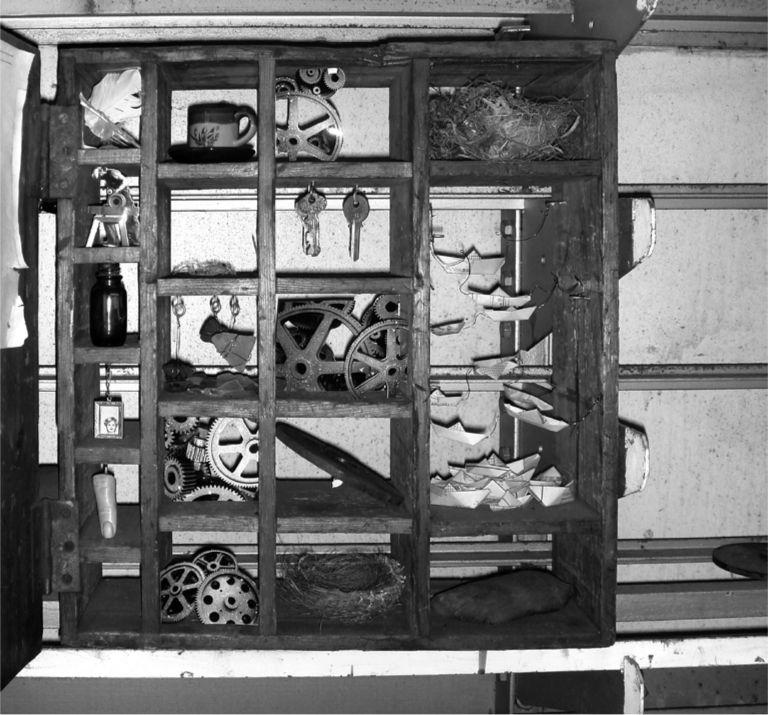 A black and white photograph of a box of random objects like wheels and keys.