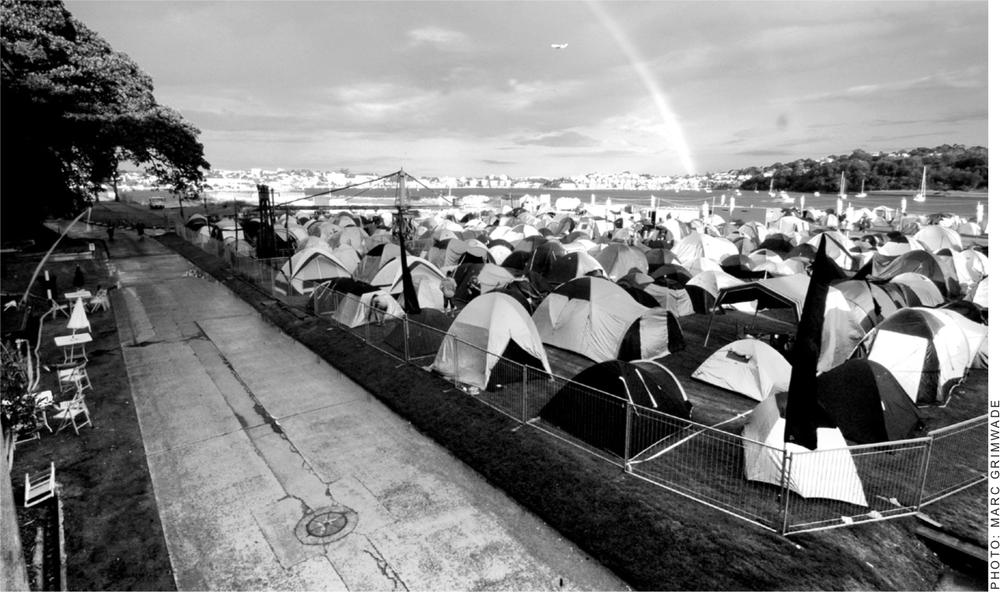 A black and white photograph of numerous tents on the grass of Cockatoo Island.