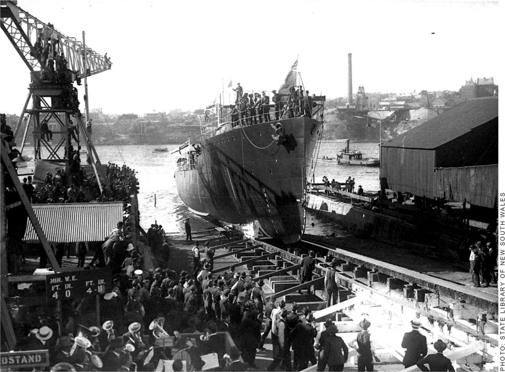 A black and white photograph of the HMAS Torrens about to leave the dock with onlookers standing on the dock.