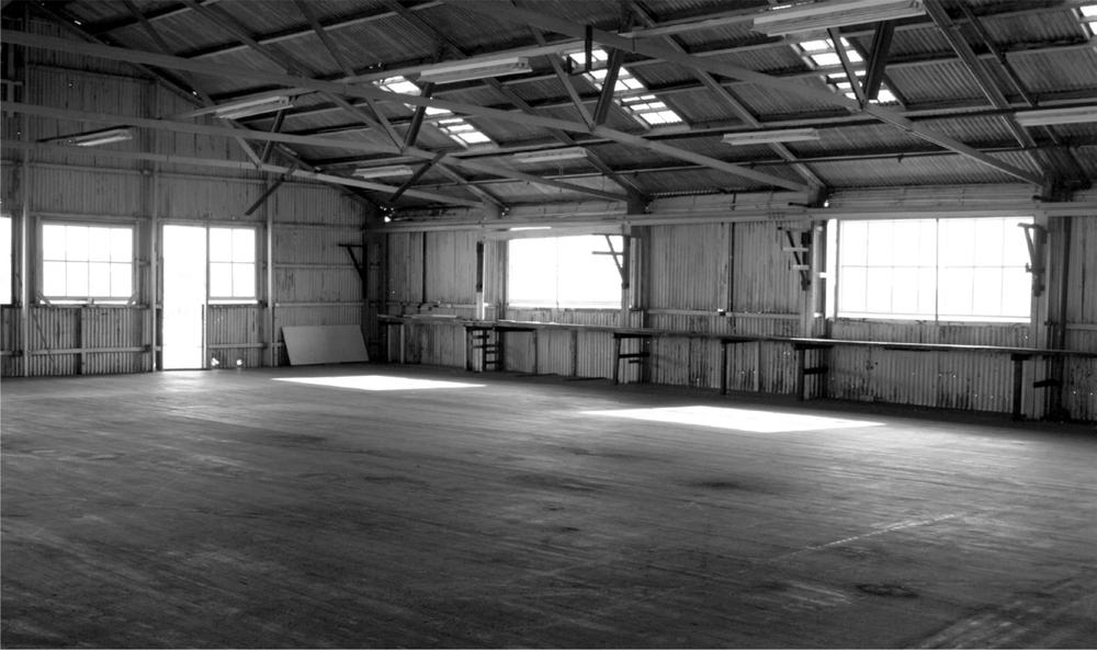 A black and white photograph of a large empty room with exposed beams.