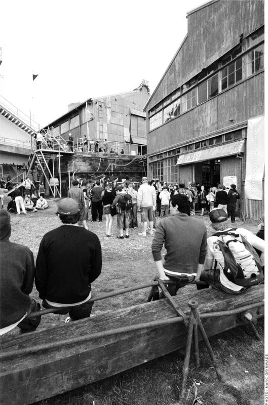 A black and white photograph of men and women outside a tin building.