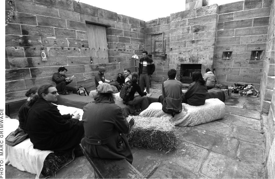 A black and white photograph of a small group of people sitting in an open area of a sandstone building.