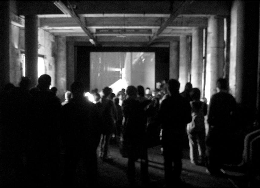 A black and white photograph of people standing in a old convict cell looking at a large screen.