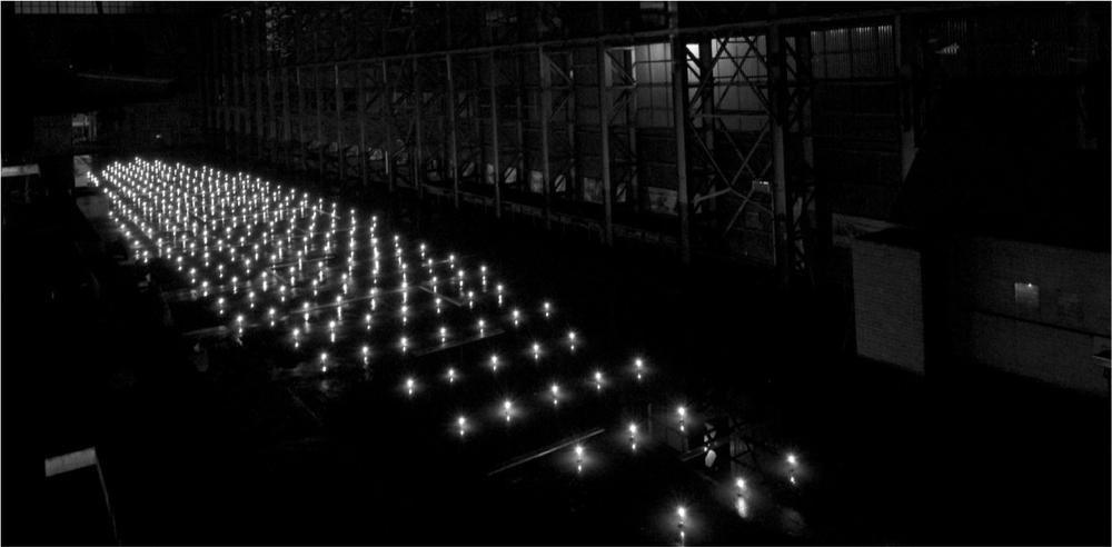 A black and white photograph of candles lit in a large room for a light installation.