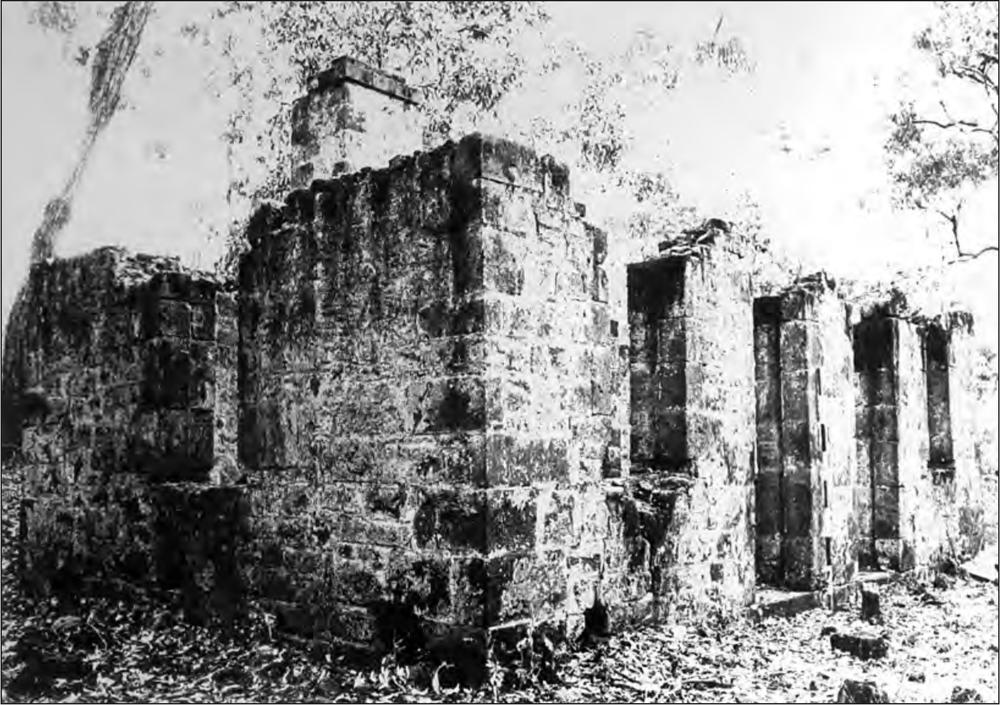 A black and white photograph of a series of thick brick columns forming a rectangle, connected by a low brick wall.