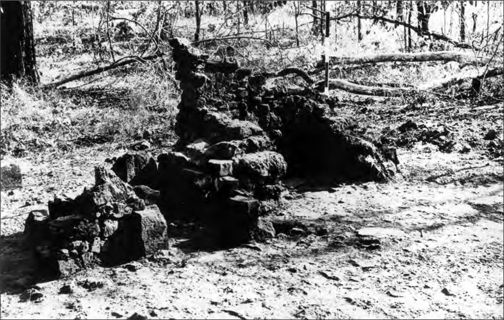 A black and white photograph of a low, broken brick wall that has a flat floor.
