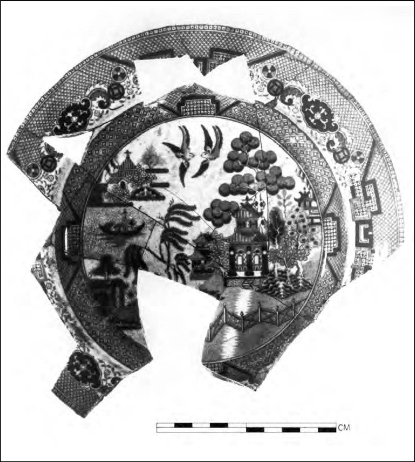A black and white photograph of a piece of pottery with missing shards. It has a circular pattern that trails around the outer rim and then another circular pattern in the middle. Within the centre circle is a print of birds, trees and a Chinese temple.
