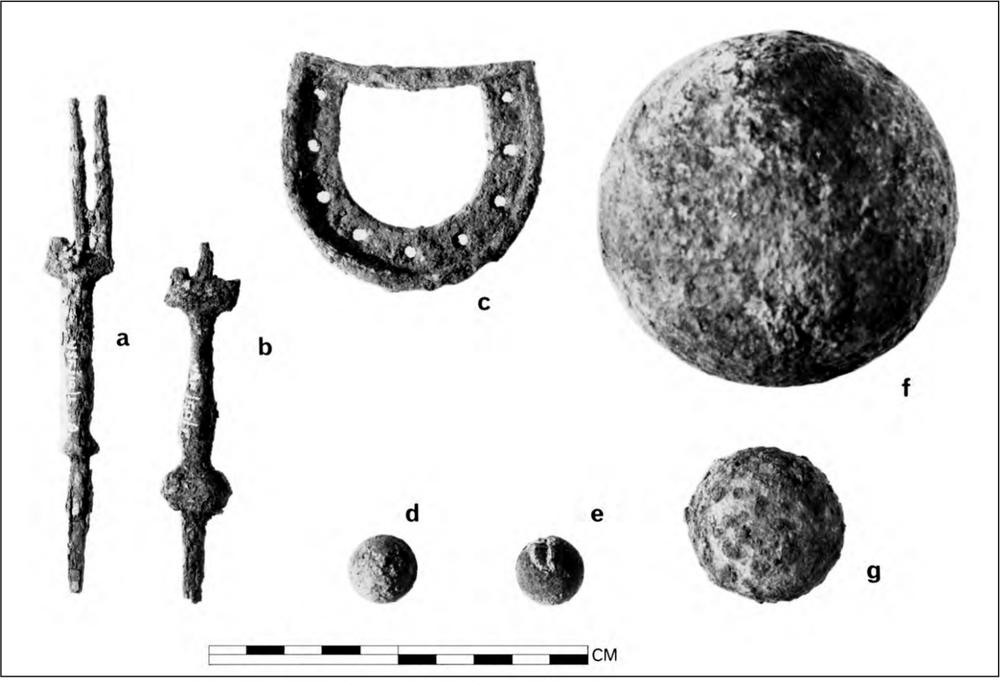 A black and white photograph of different artefacts. There are two three-tined forks that have a round bump near the end, a boot heel with holes that follow the curve of the heel, two musket balls, a cannon ball and a canister shot.