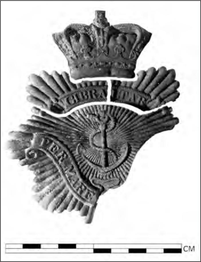A black and white photograph of a Royal Marine's officer's shake plate. It has an anchor with a rope that snakes around it at the centre and is surrounded by rays. Above it is a crown.